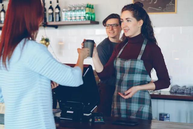 Barista serving coffee in a cafe with a QR code menu on the counter